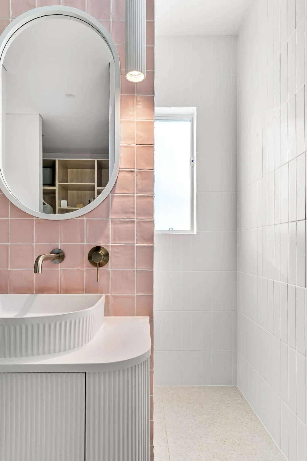 Stylish contemporary bathroom featuring a pink tile wall, oval mirror, and modern sink