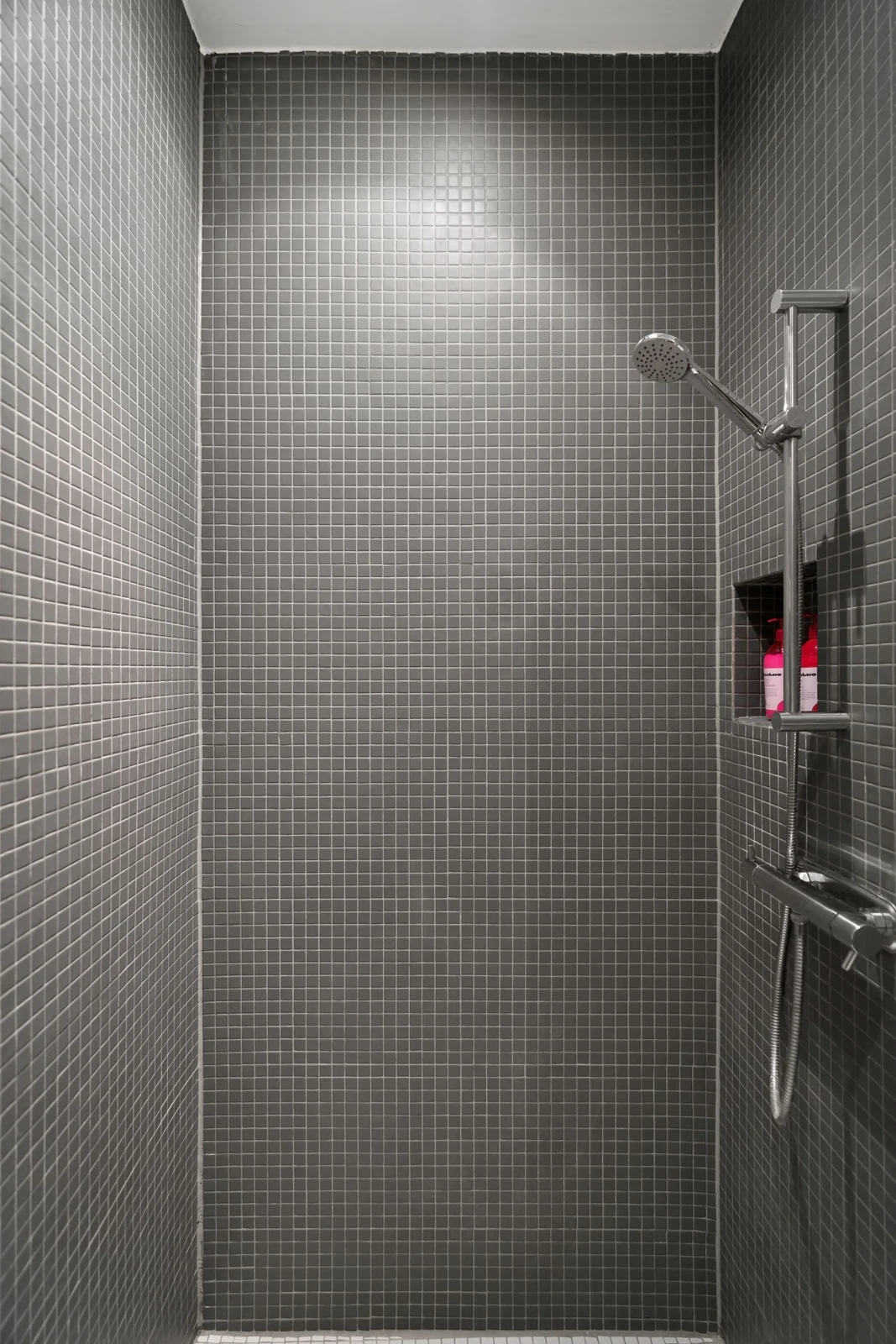 A sleek, gray tiled shower showcasing modern minimalistic design with a steel showerhead