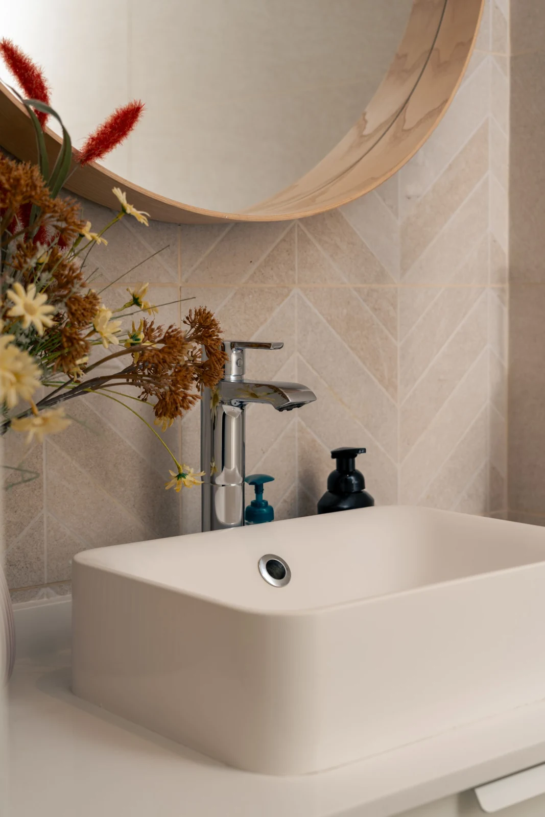 Elegant bathroom interior featuring a modern square sink, chrome faucet, and decorative flowers set against a tiled backsplash