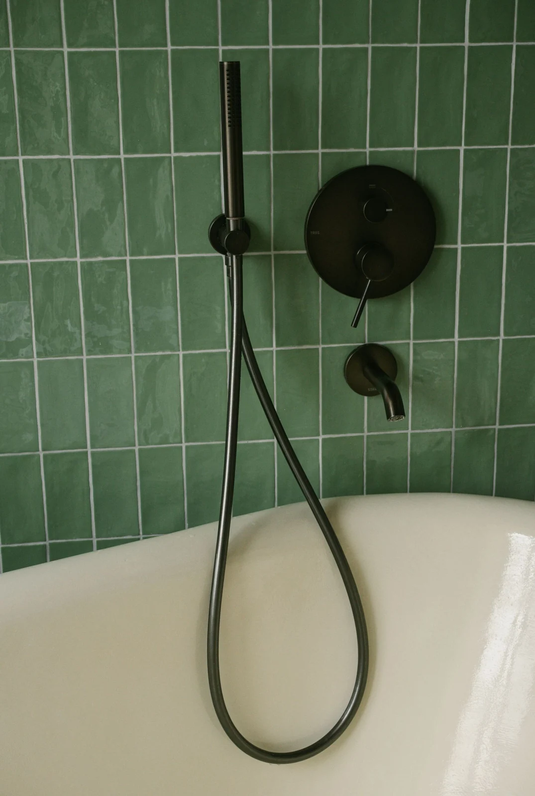 Modern bathroom featuring green tiles, a clean bathtub, and sleek black fixtures