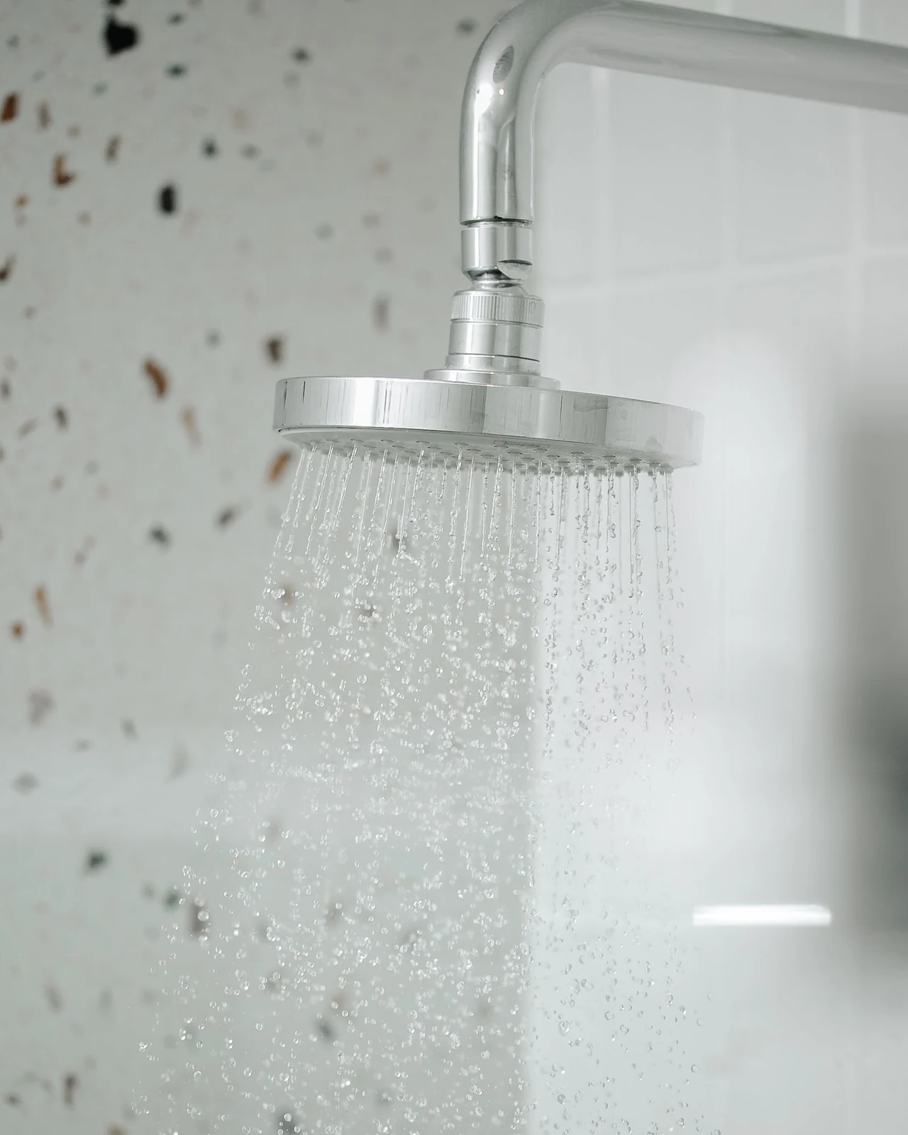 A silver shower head with water flowing in a modern bathroom setting