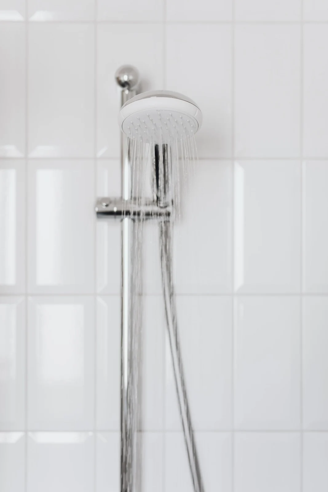 Chrome showerhead with flowing water on white tiled wall, depicting modern bathroom aesthetics